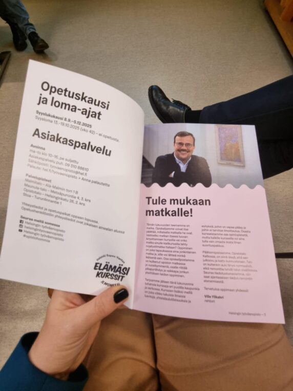 Na fotografii widoczny jest fragment ręki trzymającej broszurę w języku fińskim z ofertą kursów Fińskiego Centrum Edukacji Dorosłych w Helsinkach