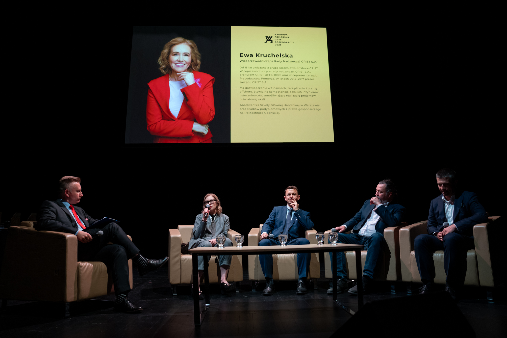 fotografia na której widać siedzących podczas debaty na scenie: od lewej: Robert Silski, moderator, Ewa Kruchelska, CRIST S.A., Łukasz Kulas, REVOBEAM/PG, Robert Magiera, SpaceForest, Maciej Włodarczyk, IGLOTEX - w tle grafika ze zdjęciem Ewy Kruchelskiej i BIO. Ewa Kruchelska trzyma w ręku mikrofon.